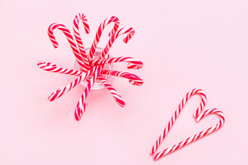Glass with sweet candy canes on pink background