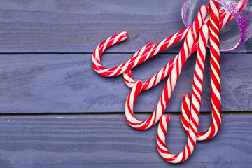 Overturned glass with sweet candy canes on color wooden background