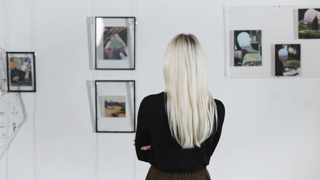 Blonde back, in the art gallery. A woman poses against the backdrop of abstract paintings by a contemporary artist.