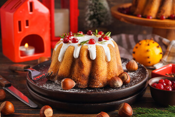 Plate with tasty Christmas cake and hazelnuts on wooden table