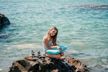 Woman with daughter bilds stones pyramid on seashore on a sunny day on the blue sea background. Happy family holidays. Pebble beach, calm sea. Concept of happy vacation on the sea, meditation, spa