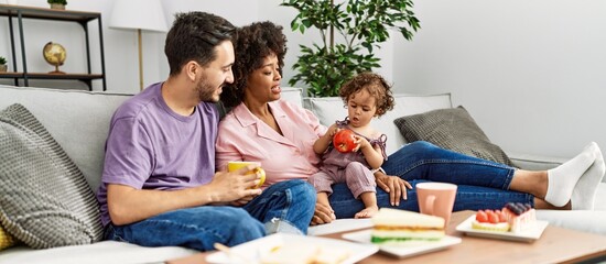 Couple and daughter having breakfast sitting on sofa at home