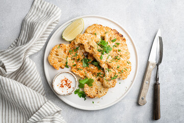 Cauliflower steaks with sauce on white plate, vegetarian dish, view from above
