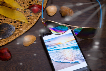 the straw hat lies on the floor in sunlight, next to the phone, shells and glasses. Holiday theme