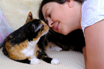 woman affectionately brings her face closer to beautiful three colors adult domestic tortoiseshell cat with white breast, relations between four-legged pets and people, beloved cat, friendship