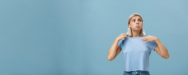 Girl feeling discomfort from heat standing over blue background in fug breathing out and frowning...