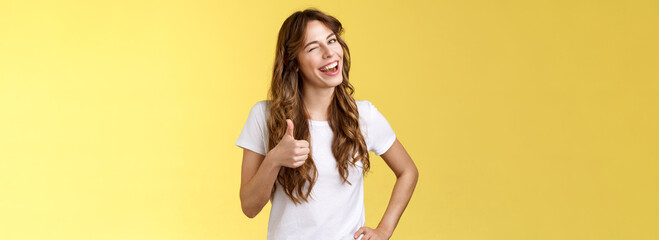 Fototapeta I support you guys good luck. Happy cheerful cheeky attractive girl wink approval like show thumb up smiling broadly satisfied awesome party congratulating friend well done yellow background obraz