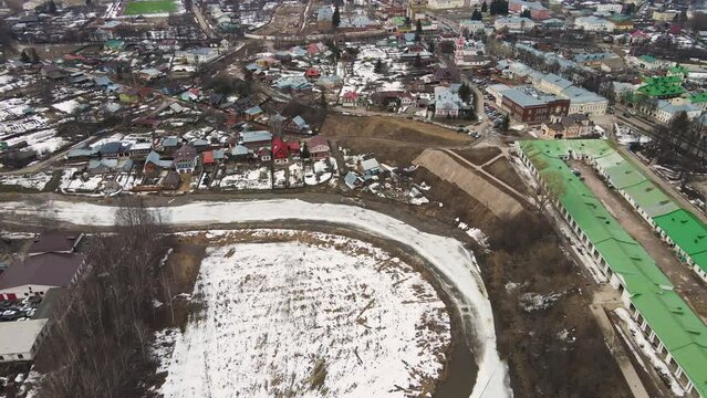 A curved frozen river, ice is melting, a small town on the shore. Spring, snow melts, dry grass, flood and river flood. Day, cloudy weather, soft warm light. UHD 4K