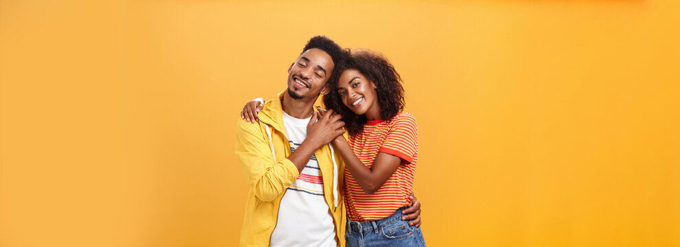 They Love Each Other. Portrait Of Two Charming African American Man And Woman In Relationship Hugging With Heartwarming Smile Touching Hands Smiling Gently Posing Against Orange Background