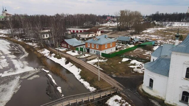 Frozen curved river with a bridge, a village on the bank. Spring, snow melts, dry grass, flood and river flood. Day, cloudy weather, soft warm light. UHD 4K
