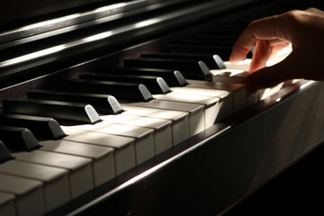 Fototapeta na wymiar Playing piano close-up shot, isolate woman hand press piano in dark background with sunlight