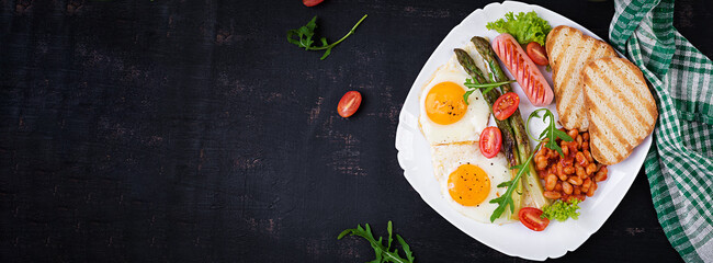 Keto breakfast. Breakfast. Fried eggs, bread toast, green asparagus, beans and sausage on white plate. Top view, banner