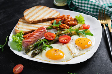 Keto breakfast. Breakfast. Fried eggs, bread toast, green asparagus, beans and sausage on white plate.