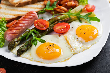 Keto breakfast. Breakfast. Fried eggs, bread toast, green asparagus, beans and sausage on white plate.