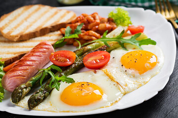 Keto breakfast. Breakfast. Fried eggs, bread toast, green asparagus, beans and sausage on white plate.