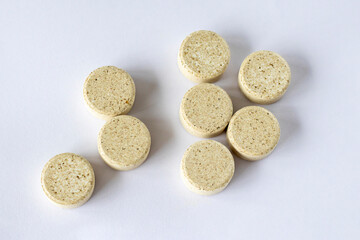 Supplements with chewable tablets DGL liquorice root. Round puck tablets of beige color with dark droplets on a white background view from above.