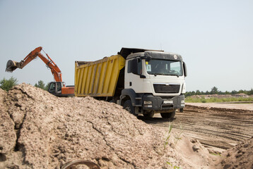construction dump truck with a yellow body and an orange crawler excavator next to each other while...
