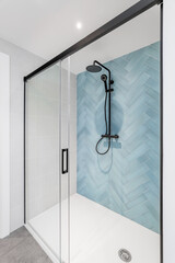 White bathroom with glass shower, walls are decorated with herringbone tiles in pale blue. Black...