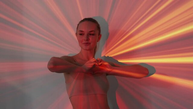 Sending love. Female silhouette portrait. Kind energy. Smiling pretty woman showing heart gesture with hands posing neon light red yellow rays double exposure background.