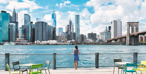 New York city Manhattan skyline seen from Brooklyn waterfront - woman looking at view. American people walking enjoying view of Manhattan over the Hudson river from the Brooklyn side. NYC cityscape - obrazy, fototapety, plakaty