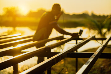 An Asian painter uses a spray gun to paint a steel frame. warm light background in the setting sun