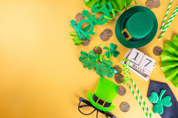 Obraz na płótnie Canvas Happy Patrick's Day greeting card, party invitation. Accessories for St Patrick holiday leprechaun hat, glasses, shamrock, gold coins, block calendar March 17 date, ornaments, gold background top view