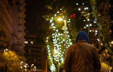 Rear view of adult man on street at night with lights of Christmas