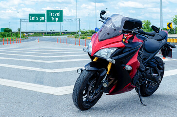 Fototapeta na wymiar Red black motorcycle modern style parked on road with message Let's go Travel Trip on green roadsign background
