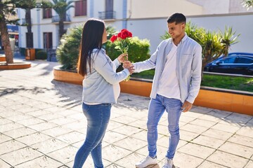 Young latin couple expecting baby surprise with flowers at park