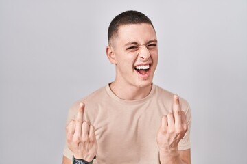 Young man standing over isolated background showing middle finger doing fuck you bad expression,...