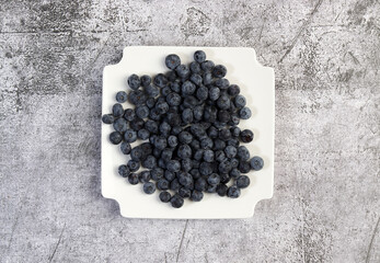 Ripe Blueberry on a white square  plate on a dark background. Top view, flat lay`