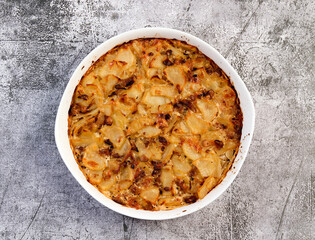 Oven baked potatoes with cheese, mushrooms and onions  in a white baking dish on a dark grey background. Top view, flat lay