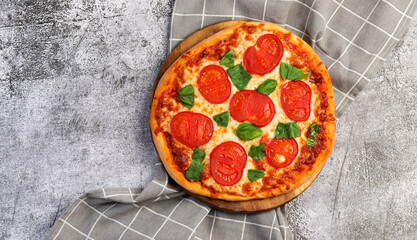 Homemade Pizza margherita with tomatoes, basil and cheese on a round wooden cutting board on a dark grey background. Top view, flat lay