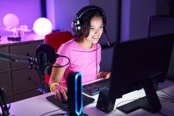 Young hispanic woman streamer playing video game using computer at gaming room