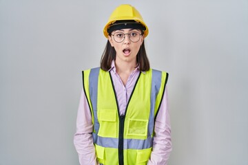 Hispanic girl wearing builder uniform and hardhat afraid and shocked with surprise expression, fear and excited face.