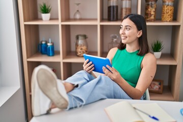 Young hispanic woman using touchpad sitting on table at home