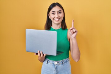 Hispanic girl working using computer laptop surprised with an idea or question pointing finger with happy face, number one