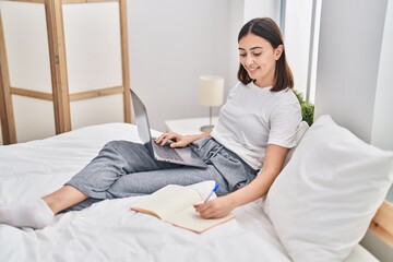Fototapeta na wymiar Young hispanic woman sitting on bed using laptop studying at bedroom