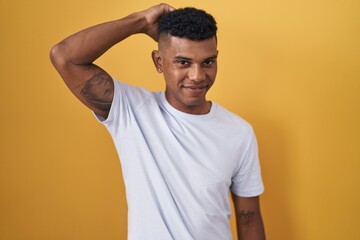 Young hispanic man standing over yellow background confuse and wondering about question. uncertain with doubt, thinking with hand on head. pensive concept.