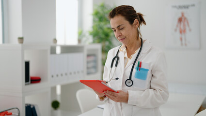 Middle age hispanic woman wearing doctor uniform using touchpad at clinic