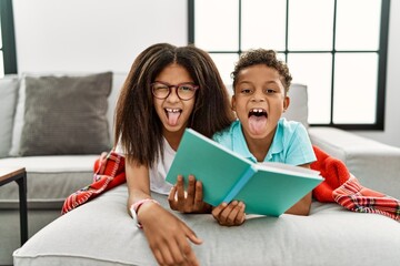 Two siblings lying on the sofa reading a book sticking tongue out happy with funny expression....