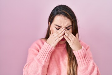 Young hispanic woman standing over pink background rubbing eyes for fatigue and headache, sleepy...