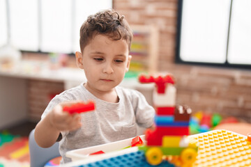 Adorable hispanic toddler playing with construction blocks sitting on table at kindergarten