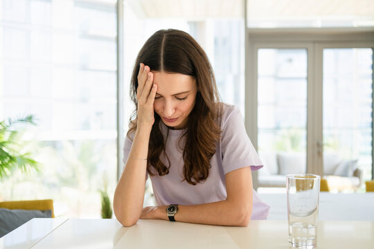 Stressed woman with head in hand leaning on table at home