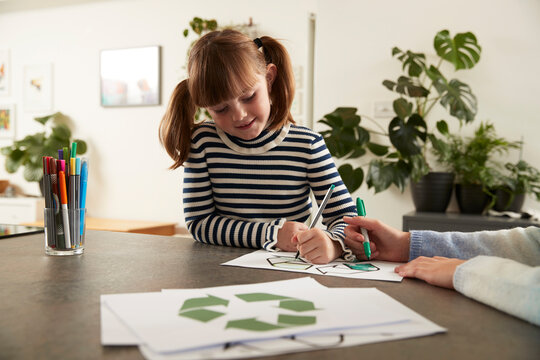 Smiling cute girl with sister coloring recycling symbol with pen at home
