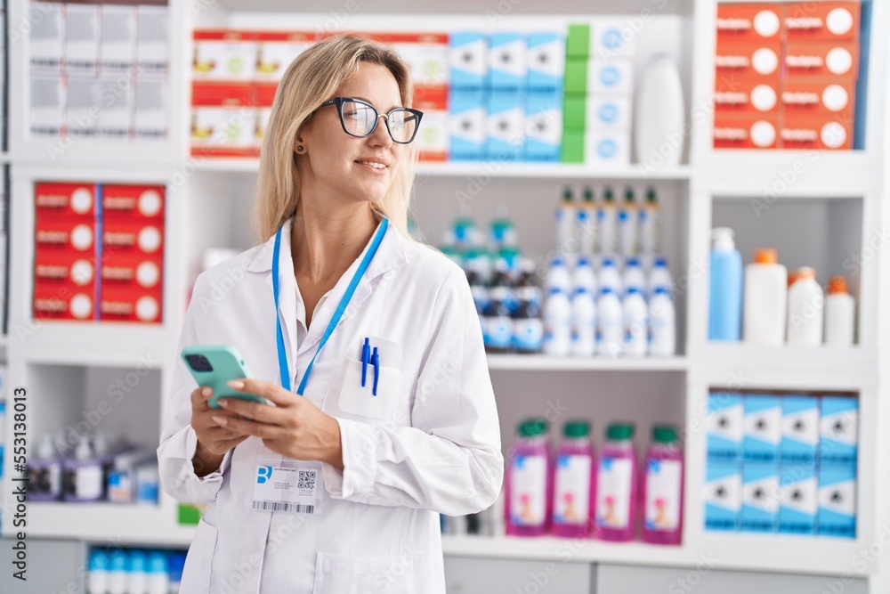 Poster young blonde woman pharmacist using smartphone working at pharmacy - Posters