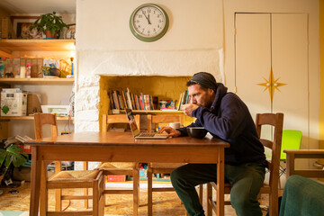 Freelancer eating meal using laptop at desk in home