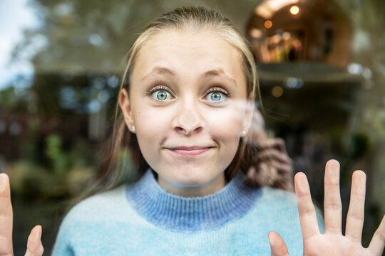 Smiling girl pressing nose on glass window
