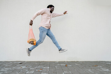 Man with grocery bag and disposable coffee cup jumping in front of white wall