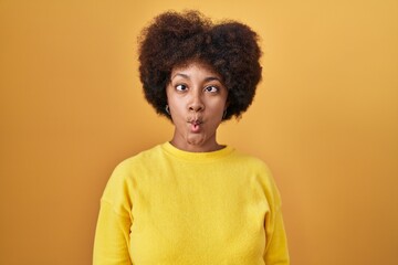 Fototapeta na wymiar Young african american woman standing over yellow background making fish face with lips, crazy and comical gesture. funny expression.